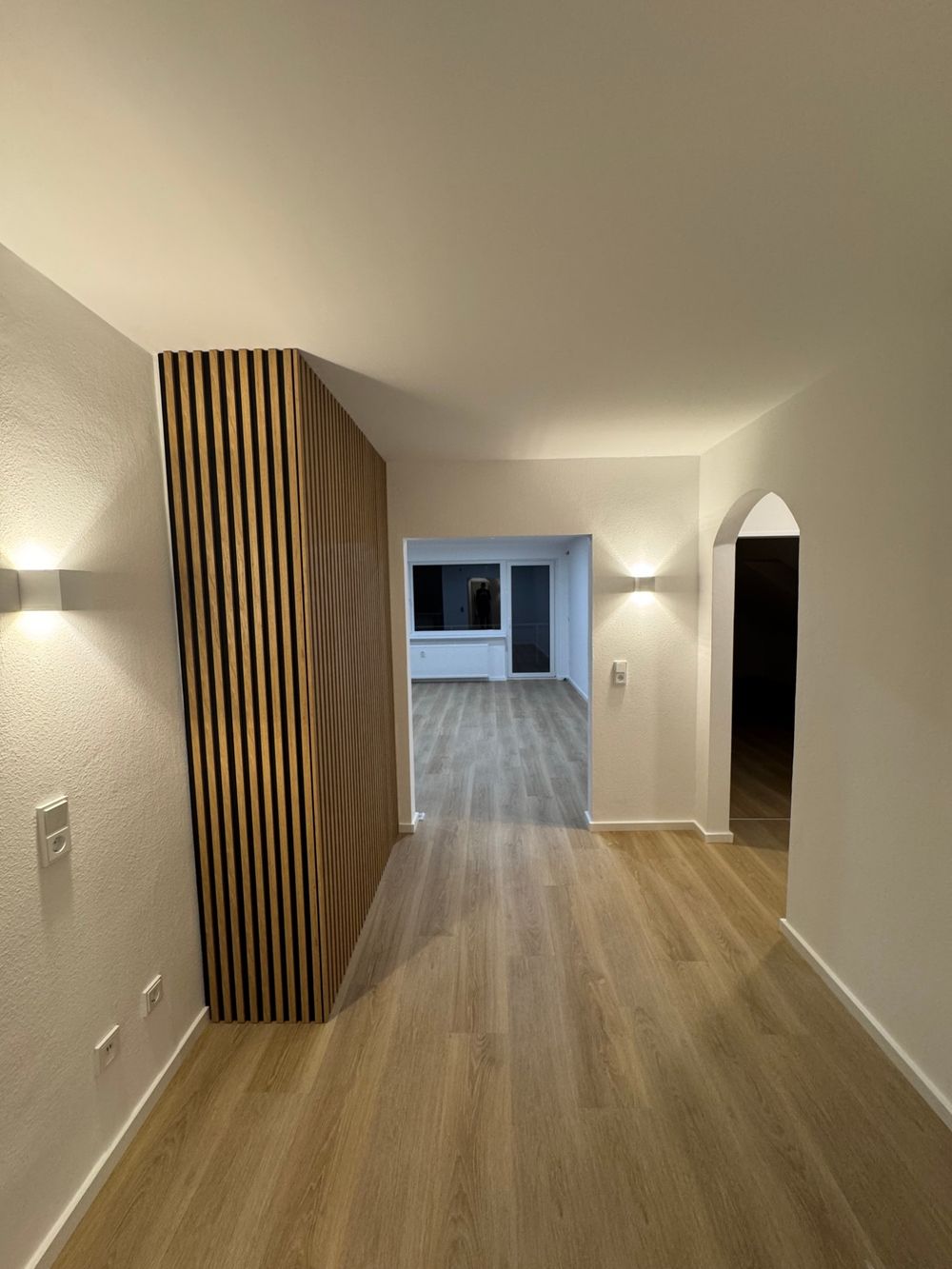 Frisch renovierter Flur mit neuem Boden, Wandleuchten und Blick in den hellen Wohnraum